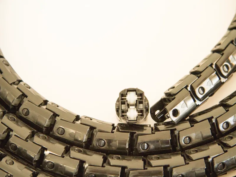 Rolliner conduit section coiled into a ring, showing the linked chain of roller modules from above; one snap element is separated open in the foreground